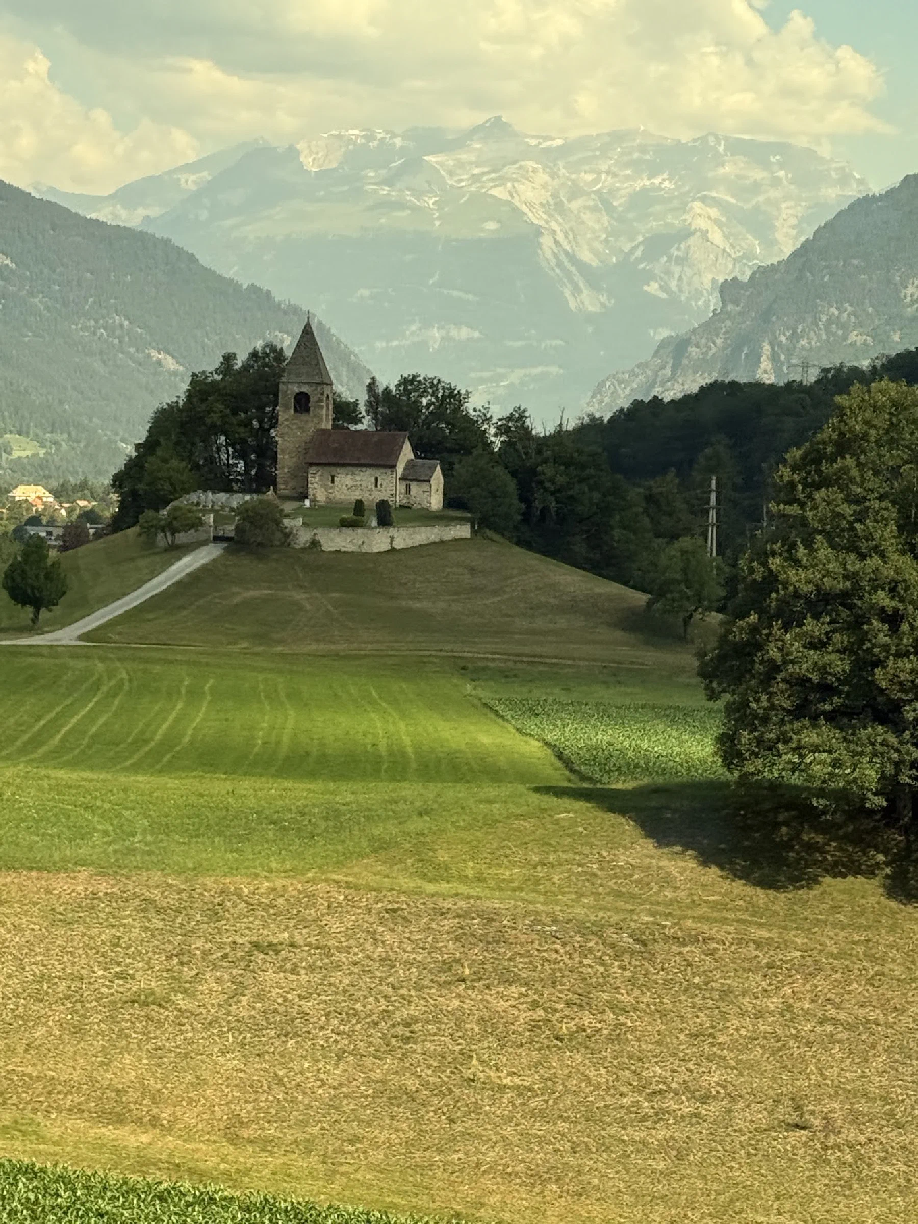 A small stone church on a green hillside with mountains rising behind it