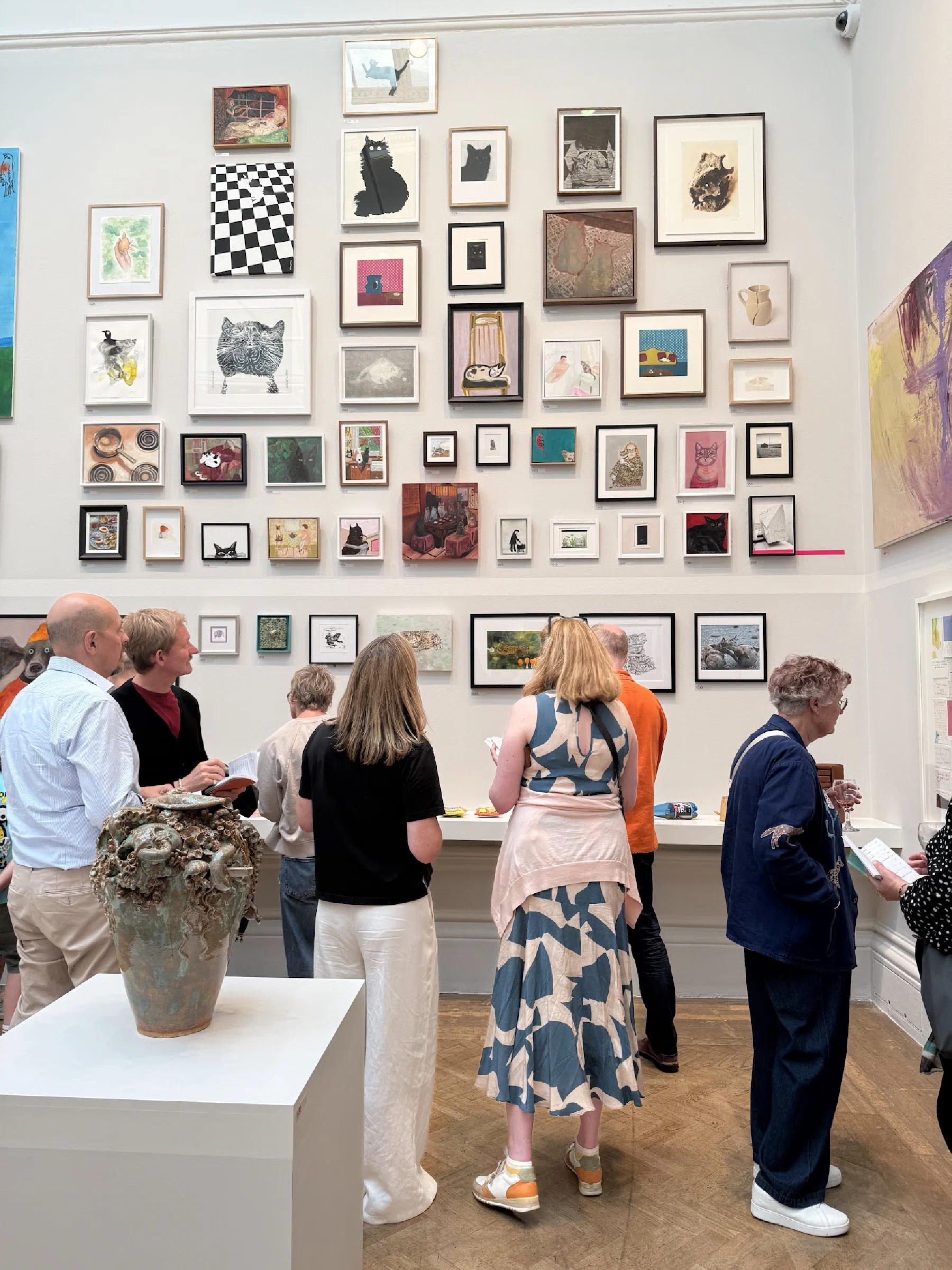 Visitors gathered in a gallery beneath a wall filled with small artworks of cats