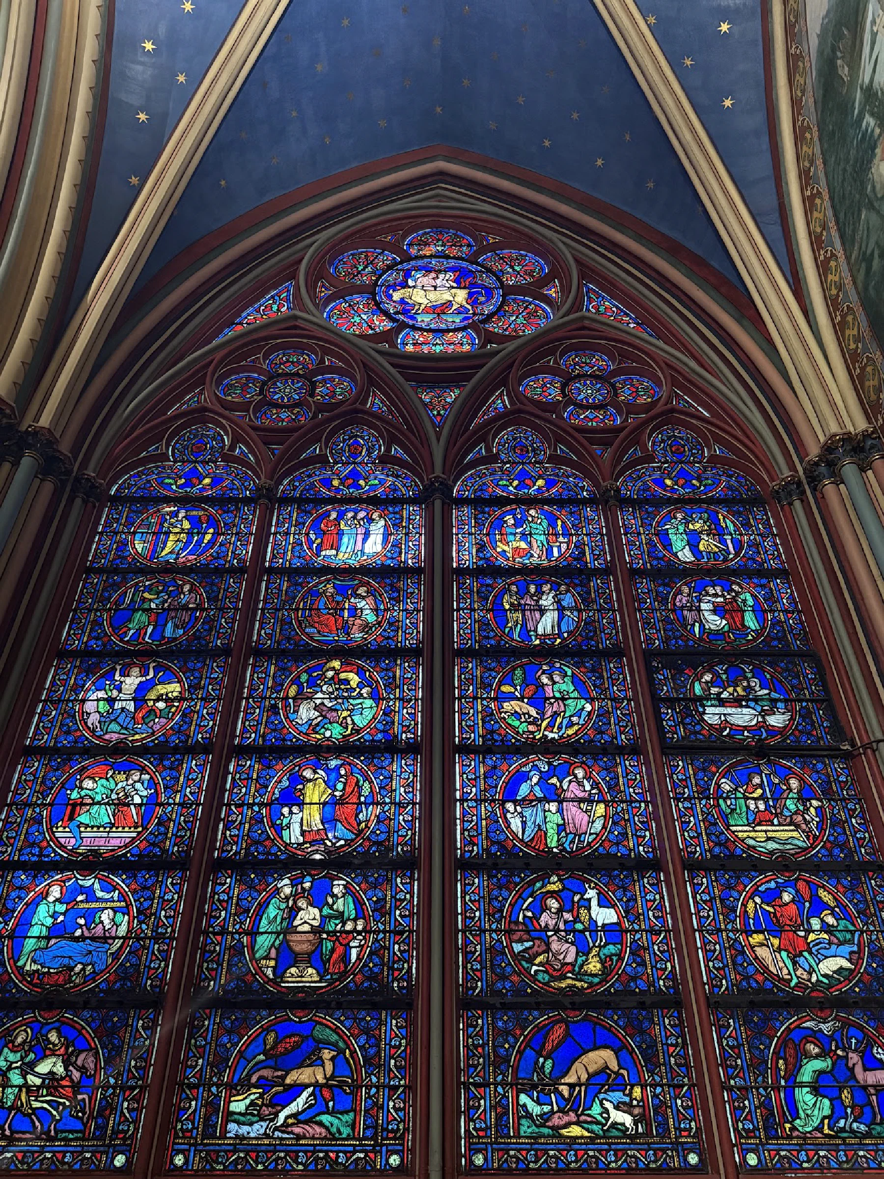 A tall stained-glass window beneath a blue vaulted ceiling dotted with gold stars